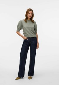 Maglione verde chiaro lavorato a maglia con maniche corte a sbuffo, abbinato a jeans a gamba larga blu scuro. L'outfit è completato da ballerine beige con punta.