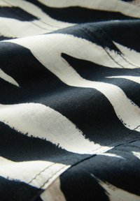 Stof met een gedurfde zwart-witte zebra-print; gladde textuur met zichtbare stiksels langs de randen.