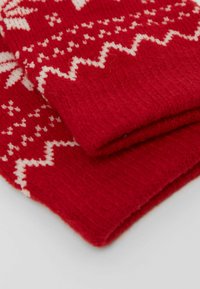 Muffole rosse lavorate a maglia con motivi geometrici bianchi, caratterizzate da una texture morbida e polsini a coste, sovrapposte leggermente.