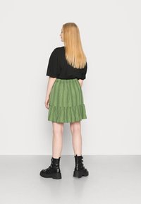 Saia verde em camadas com riscas verticais, blusa preta folgada e botas pretas com atacadores e detalhes metálicos. Vista pela parte de trás.