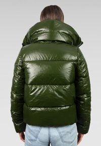 Groene pufferjas met een glanzende afwerking, met een hoge kraag en gequiltte secties. Het ontwerp is cropped op de taille en wordt gecombineerd met blauwe jeans.