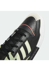 Svart sneaker med ovandel i läder, med gröna ränder, en texturerad tåhätta och en vit sula. Inkluderar svarta snören och accentstickningar.