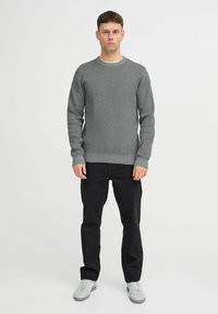 Maglione grigio a maglia con colletto rotondo, polsini e vita a costine, abbinato a pantaloni neri e scarpe da ginnastica grigie. Vestibilità casual e design testurizzato.
