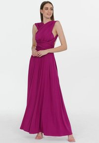 Dlouhá, splývavá večerní šaty v fuchsiové barvě s detailním zvratem v oblasti dekoltu a bezramenným designem. Hladká textura s dlouhým siluetou až na zem.
