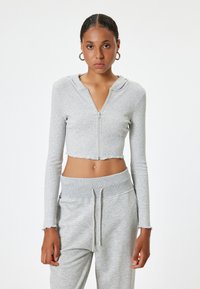 Lichtgrijze cropped zip-up hoodie met lange mouwen, ribbeltextuur en onafgewerkte zoomdetails, gecombineerd met bijpassende sweatpants in dezelfde kleur.