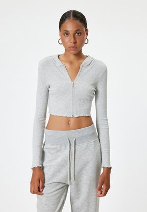 Lichtgrijze cropped zip-up hoodie met lange mouwen, ribbeltextuur en onafgewerkte zoomdetails, gecombineerd met bijpassende sweatpants in dezelfde kleur.
