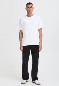 Tricou alb cu mâneci scurte asortat cu pantaloni negri din catifea cu dungi. Pantalonii au o textură nervurată, iar pantofii sunt albi cu dungi negre.