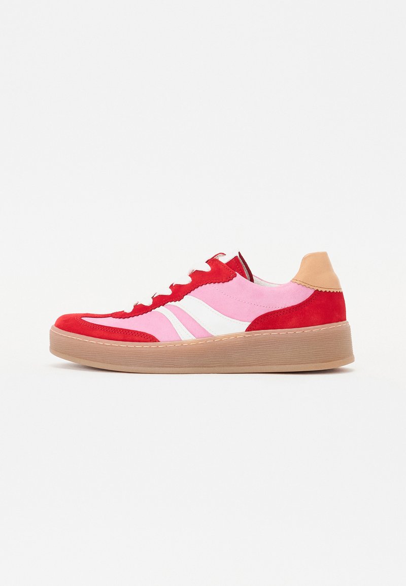 Sneaker in suede rosso e rosa con strisce bianche, parte superiore testurizzata, collo imbottito e tallone beige, poggiata su una suola in gomma marrone.