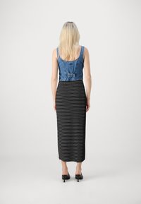 Denim skrčen vrh s prilagojenim pasom in podrobnostjo z zaponko na hrbtu, v kombinaciji z dolgo črno krilo, ki ima bele vodoravne črte in pete.