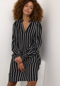 Schwarz-weißer gestreifter Kleid mit V-Ausschnitt, langen Ärmeln und gesmokten Bündchen. Aus leichtem Stoff, fällt oberhalb der Knie.