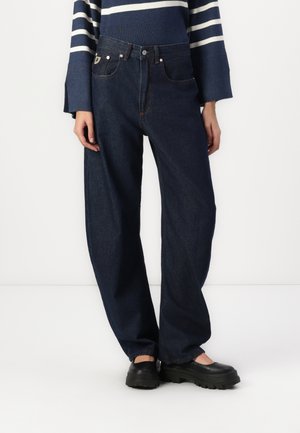Jeans din denim de culoare albastru închis, cu croi larg, cinci buzunare, închidere cu nasture și cusături contrastante de culoare portocalie. Purtați cu un pulover în dungi navy.