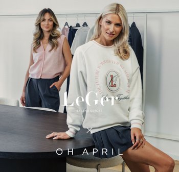 Weisses Sweatshirt mit pinkem Logo und Text, kombiniert mit einem grauen Rock. Das Model trägt eine hellpinke Weste und steht hinter einem dunklen Holztisch.