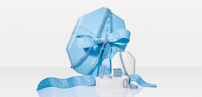 Blue crystal jewelry set including necklace, bracelets, and rings displayed with a blue Swarovski ribbon and gift box.