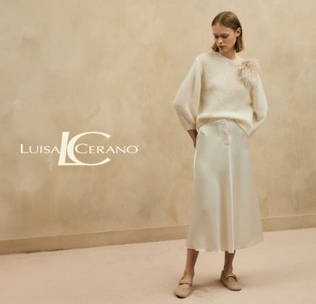 Cream sweater with textured knit and a feather accent, paired with a white satin midi skirt and beige woven loafers. Soft, neutral palette.