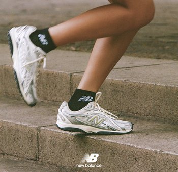 Witte en zilveren hardloopschoenen met een gestructureerd ontwerp, logo-accenten en zwarte sokken, gepositioneerd op trappen, die beweging benadrukken.
