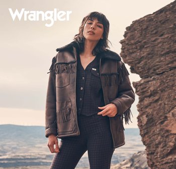 Brun skinnjakke med frynse detaljer, svart kunstig pelskrage, frontlommer og glidelåslukking, båret med en teksturert, mørk antrekk.