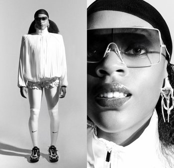 Chaqueta blanca plisada con un cuello alto, combinada con pantalones cortos texturizados y leggings blancos, acentuada por gafas de sol de gran tamaño y pendientes llamativos.