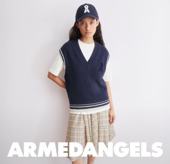 Gilet senza maniche lavorato a maglia blu navy con scollo a V e dettagli a righe bianche, abbinato a una t-shirt bianca e una gonna a quadri. Il berretto presenta un logo.