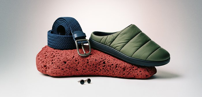 Πράσινο παπούτσι τύπου slip-on με ραφή, περιτυλιγμένη μπλε θάλασσα υφασμένη ζώνη με μεταλλική αγκράφα και στρογγυλά μαύρα μανικετόκουμπα τοποθετημένα πάνω σε πορώδες κόκκινο πέτρωμα.