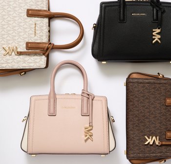 Cuatro bolsos Michael Kors en beige, negro, rosa claro y marrón con el característico charm del logo MK en dorado sobre un fondo blanco.