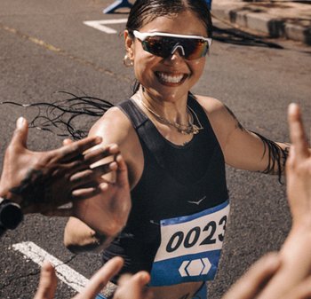 Atleta che indossa una canotta nera e occhiali da sole riflettenti, con il numero '0023' su un pettorale blu, che si scambiano un cinque in un contesto di gara.