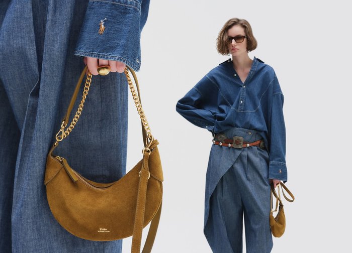 Persona vistiendo una camisa y pantalones de mezclilla extragrandes, sosteniendo un pequeño bolso de ante marrón con cadena dorada, posando frente a un fondo liso.