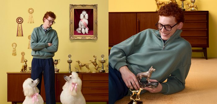 Άνδρας με κόκκινα μαλλιά και γυαλιά ποζάρει με δύο λευκούς κούρελους που φορούν ροζ φιόγκους, περιτριγυρισμένος από κύπελλα σκύλων και ένα κορνιζαρισμένο πορτρέτο κούρελου.