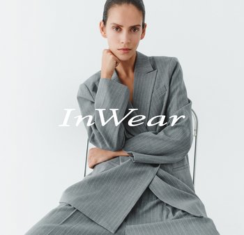 Grauer Nadelstreifen-Blazer und Hose aus einem maßgeschneiderten Stoff. Das Modell sitzt und posiert vor einem minimalistischen Hintergrund, der die Details des Outfits hervorhebt.