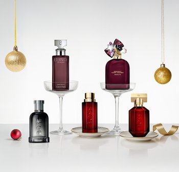 Fem parfymflaskor i olika former och färger: klar, svart och djupröd glas, utställda på pelare med gyllene accenter och dekorativa ornament.