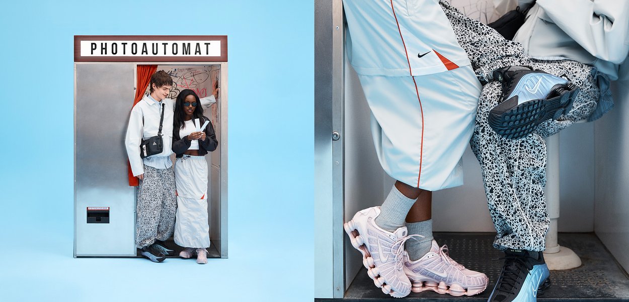 Dos personas de pie dentro de una cabina fotográfica vintage etiquetada como PHOTOAUTOMAT, vistiendo pantalones estampados y zapatillas casuales.