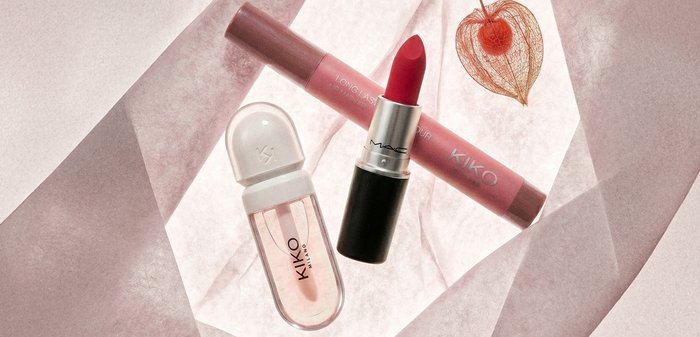 Rouge à lèvres rouge, crayon à lèvres rose et vernis à ongles transparent disposés sur un tissu rose doux avec une délicate coque d'angélique orangée.