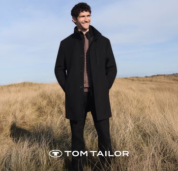 Czarny płaszcz z wysokim kołnierzem, zapinany na guziki, z boczną kieszenią, nałożony na brązowy sweter w wzory i czarne spodnie.