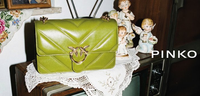 Borsa verde in pelle con fermaglio a forma di uccello dorato su centrino all'uncinetto sopra una TV vintage, circondata da statuette di angeli in porcellana e fotografie incorniciate.