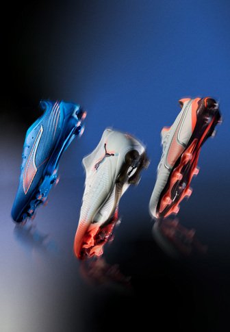 Trois chaussures de football exposées : une chaussure bleue au design épuré, une chaussure grise avec des accents rouges, et une chaussure noire avec des accents orange.