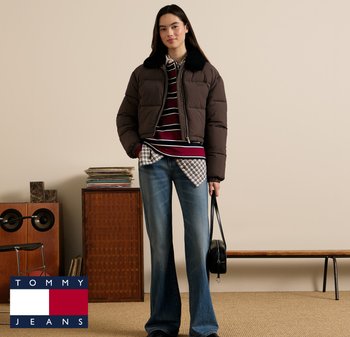 Ciemnobrązowa pikowana kurtka z czarnym kołnierzem, nałożona na nią pasiasta koszula, pod którą jest koszula w kratę, do tego rozszerzane niebieskie dżinsy i czarna torba.