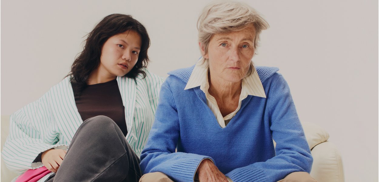 Kaksi henkilöä istuu vierekkäin vaalean värisessä sohvasohvassa. Toinen on pueta sininen villapaita valkoisen kauluspaidan päälle; toinen on raidallisessa kylpytakissa.