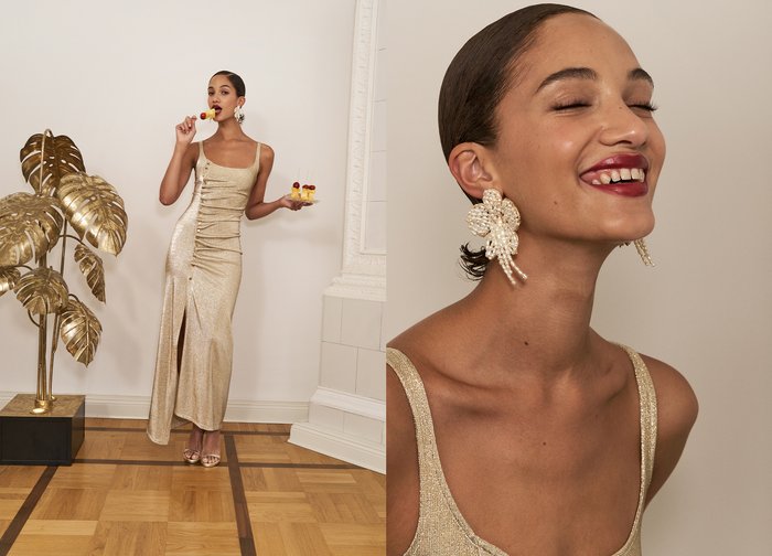 Gold, figure-hugging dress with ruched details and a side slit. The model is holding a dessert, wearing large pearl-embellished earrings and strappy sandals.