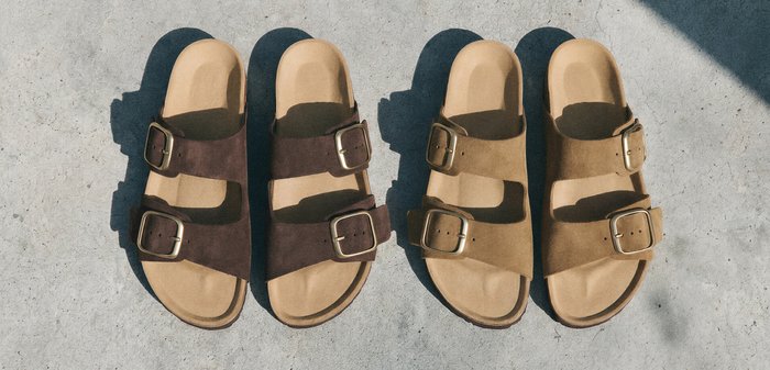 Two pairs of open-toe sandals with double buckle straps, one dark brown and one light brown, placed side by side on a concrete surface.