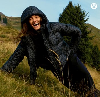 Zwarte pufferjack met een subtiele luipaardprint, voorzien van een capuchon, geborduurde textuur, en gedragen over zwarte broeken in een graslandschap.