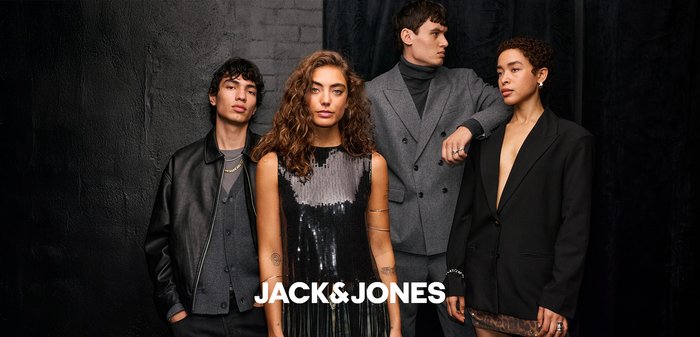 Juodas aksominis švarkas ant baltos marškinėlių, papildytas juodais saulės akiniais. Foną sudaro tamsi spalva, kuri paryškina drabužių savybes.