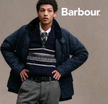 Navy quilted jacket with a high collar, layered over a dark sweater with a geometric pattern; charcoal gray trousers and black belt.