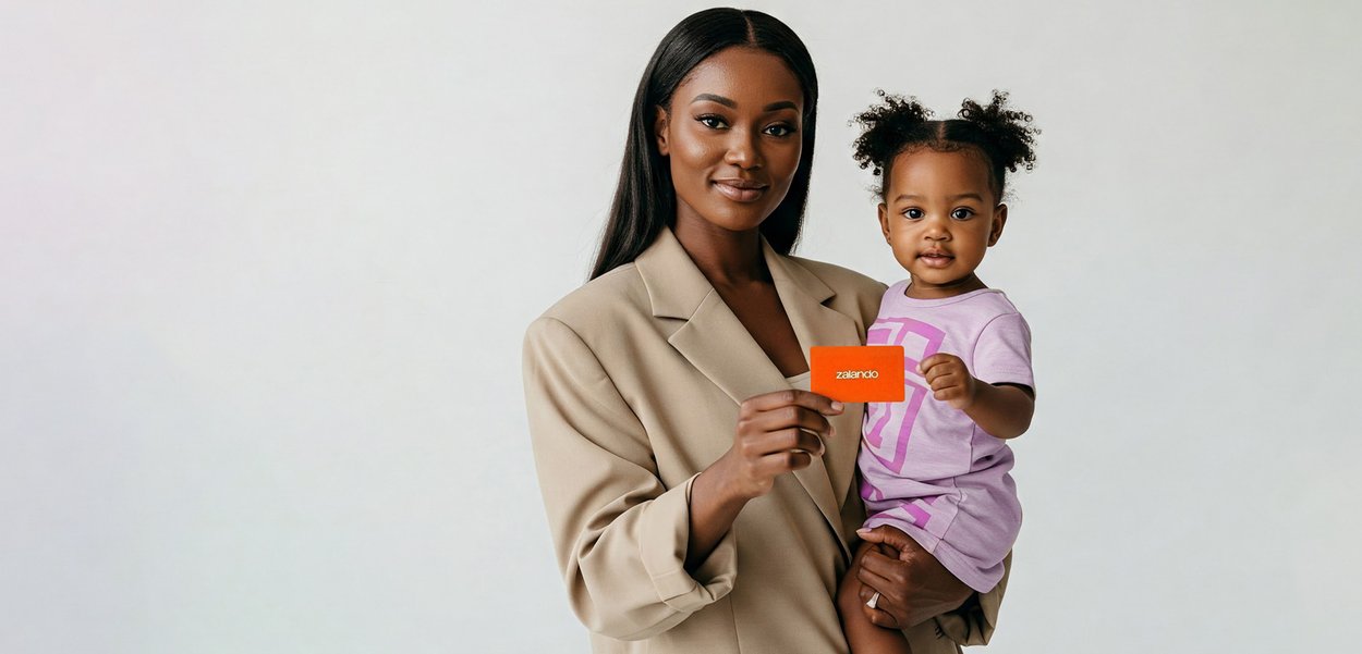 Femme tenant un tout-petit, tous deux regardant la caméra ; la femme tient une carte orange Zalando sur un fond clair uni.