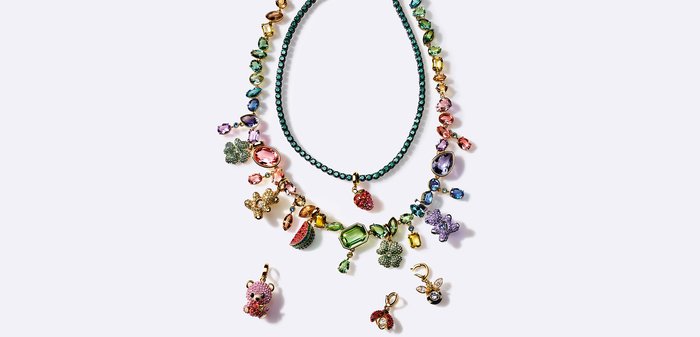 Deux colliers colorés en perles avec des charms en pierres précieuses comprenant des fleurs, des animaux, des fruits, et un pendentif fraise sur fond blanc.