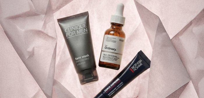 Gel nettoyant visage Clinique, sérum The Ordinary avec compte-gouttes, et sérum pour les yeux Biotherm Homme sur un fond en papier texturé rose pâle.