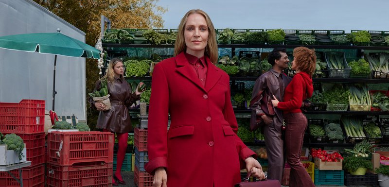 Manteau rouge avec boutons au premier plan ; le fond du marché vert présente des cagettes de légumes et deux couples interagissant à proximité.