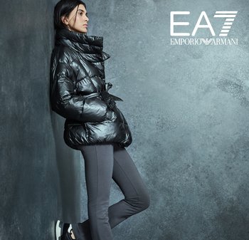 Doudoune noire avec un col haut et des détails zippés, associée à des leggings gris et des baskets noires avec une semelle blanche.