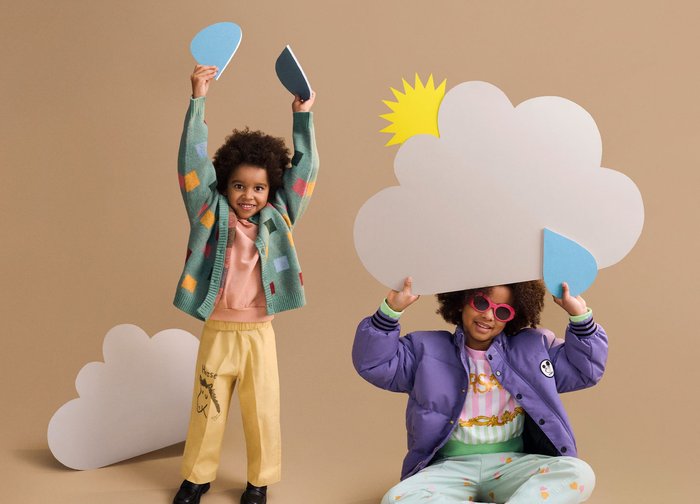 Deux enfants jouent avec des découpages sur le thème de la météo ; l'un tient des panneaux en forme de nuage et de goutte de pluie, l'autre lève des formes bleues, tous deux sourient à l'intérieur.