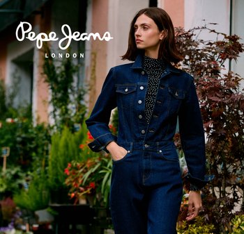 Macacão de ganga azul escuro com design ajustado, grandes botões frontais, bolsos no peito e mangas compridas. Camisola de gola alta preta com bolinhas por baixo.