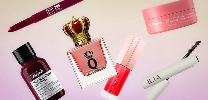 Lip liner pencil, color serum, perfume with crown cap, lip gloss, eye patches, and mascara arranged on light surface.