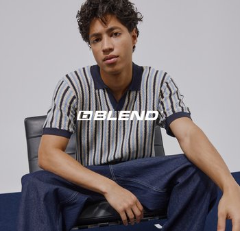 Jonge man zittend op een zwarte stoel, gekleed in een gestreept poloshirt en blauwe jeans, met het logo "BLEND" op de borst.